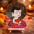 Decorative item of a cartoon-like Buddha figure on a lotus with candles and flowers in the background