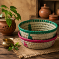 Stack of woven baskets with green and pink accents on a wooden surface with decorative items.