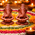 Three terracotta Ganesh statues on a floral布置 with lit candles in the background