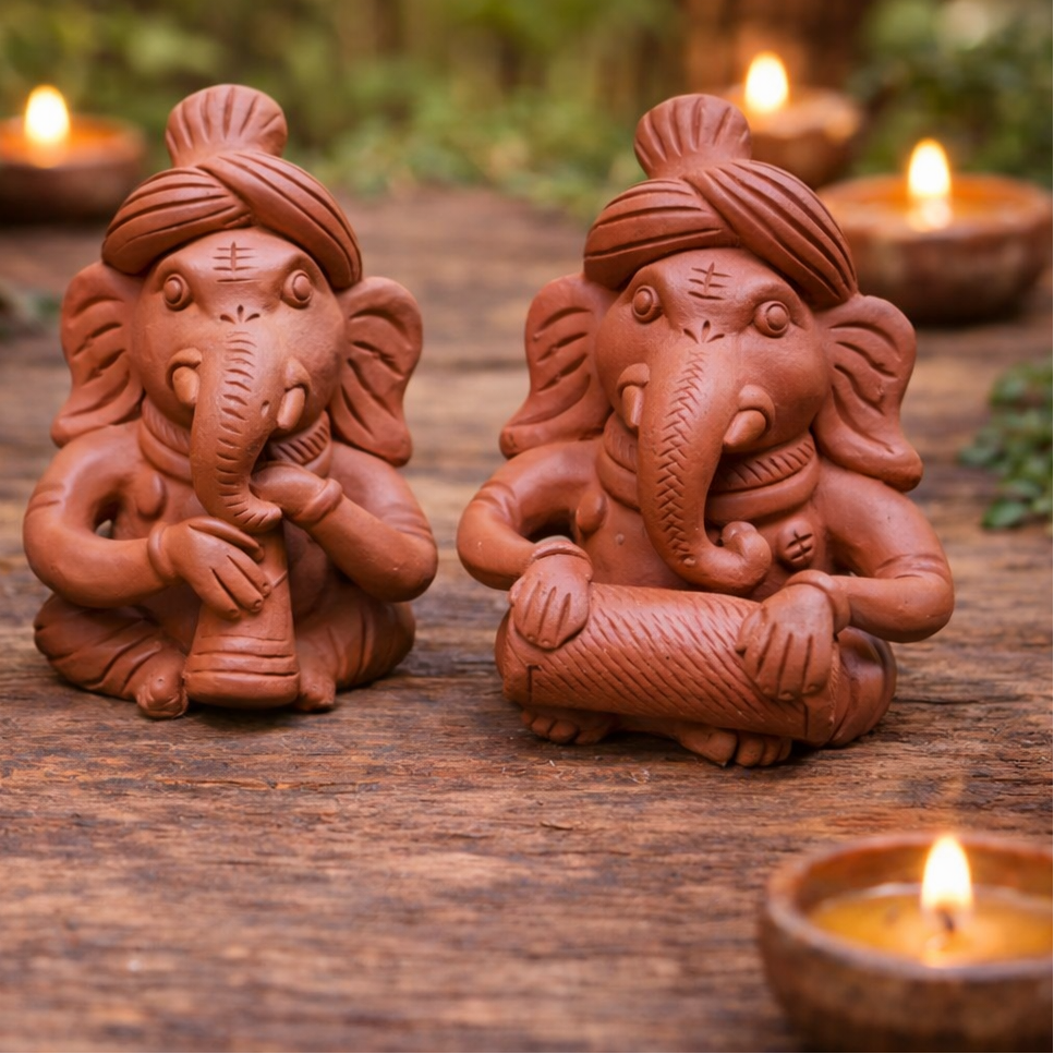 Three terracotta Ganesh statues on a wooden surface with lit candles in the background.